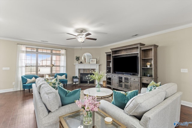 living room featuring a tiled fireplace, dark hardwood / wood-style flooring, ornamental molding, and ceiling fan