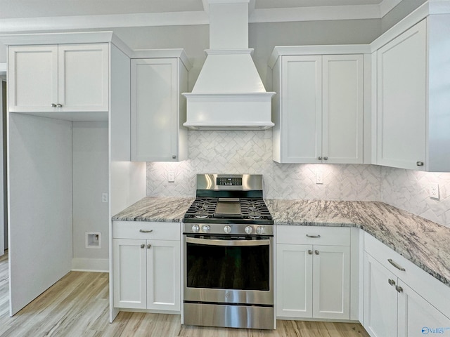 kitchen featuring tasteful backsplash, premium range hood, light wood-type flooring, stainless steel gas range oven, and white cabinetry