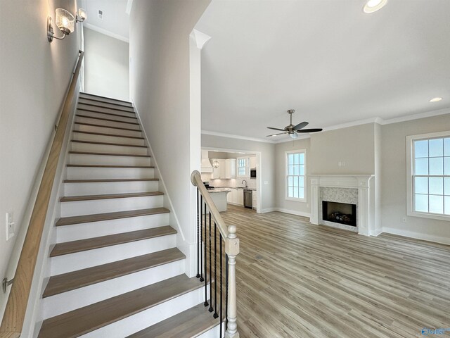 stairway featuring hardwood / wood-style floors, crown molding, a premium fireplace, and a wealth of natural light