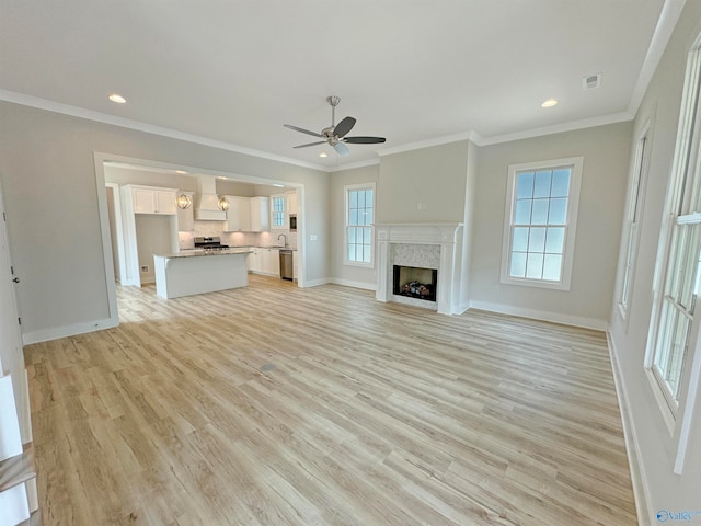 unfurnished living room with sink, crown molding, light wood-type flooring, and ceiling fan