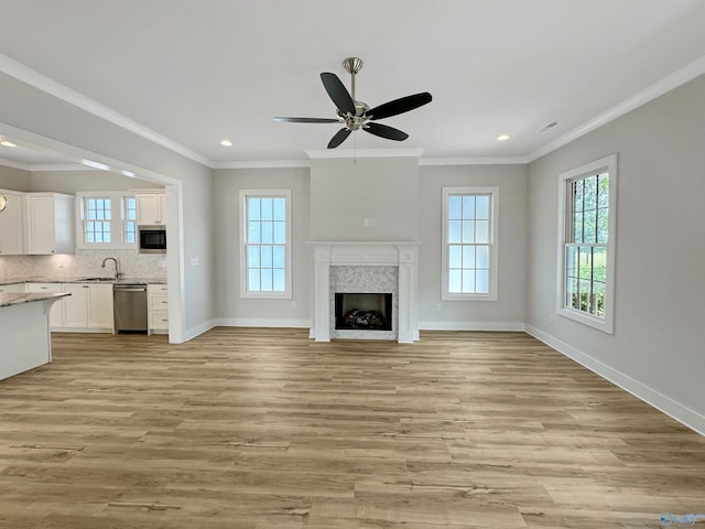 unfurnished living room featuring sink, ceiling fan, a high end fireplace, crown molding, and light hardwood / wood-style flooring