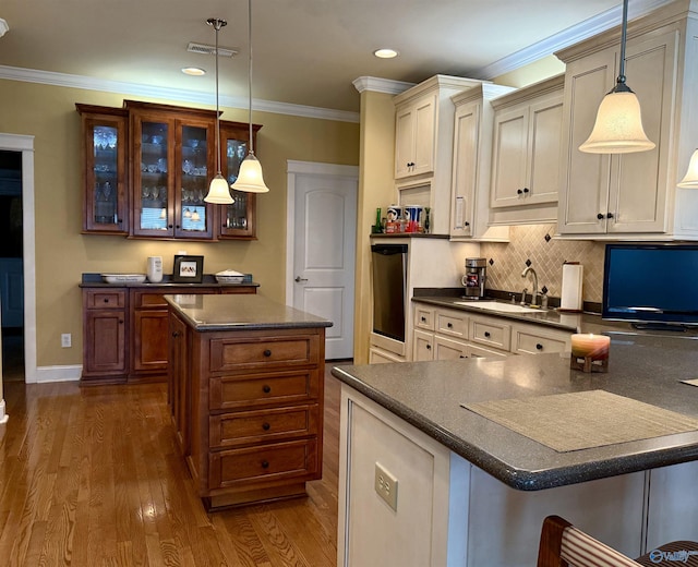 kitchen featuring a sink, glass insert cabinets, dark countertops, and visible vents