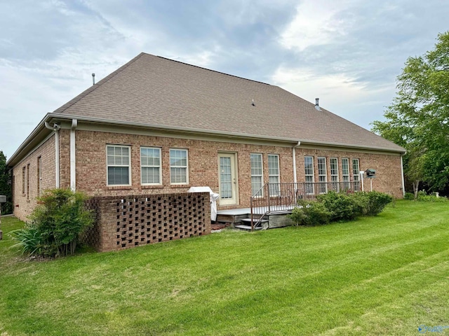 rear view of property featuring a yard, roof with shingles, a wooden deck, and brick siding