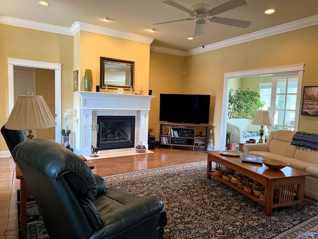 living area with ornamental molding, a glass covered fireplace, ceiling fan, and wood finished floors