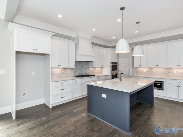 kitchen with hanging light fixtures, a kitchen island with sink, custom range hood, and white cabinets