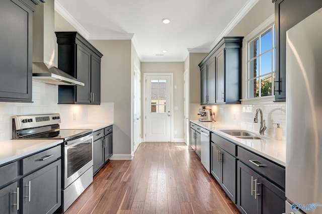 kitchen with dark wood finished floors, a sink, light countertops, appliances with stainless steel finishes, and wall chimney exhaust hood