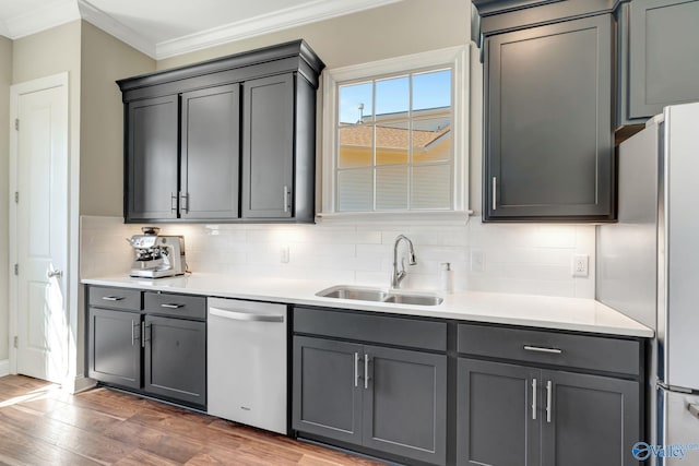 kitchen with ornamental molding, a sink, wood finished floors, stainless steel appliances, and decorative backsplash