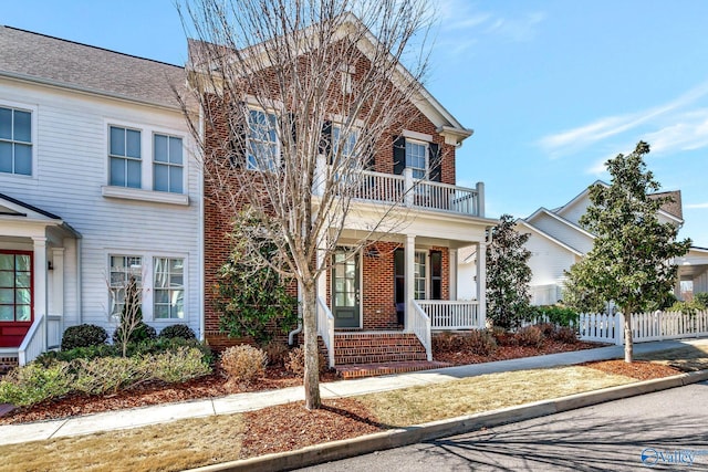 multi unit property featuring brick siding, a porch, a balcony, and fence