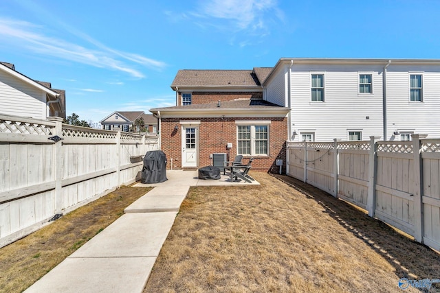 back of house featuring brick siding, a patio area, a yard, and a fenced backyard