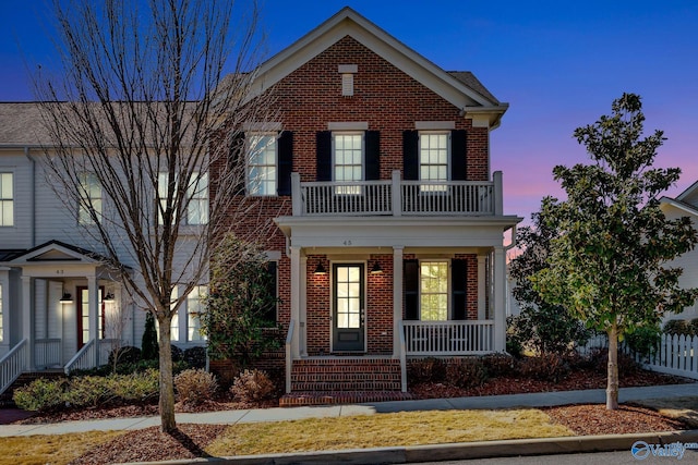 view of front facade featuring a balcony, fence, covered porch, and brick siding