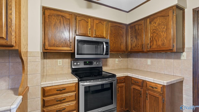 2302 Auburn Dr, Decatur, AL 35603 - kitchen featuring stainless steel appliances, decorative backsplash, brown cabinets, and ornamental molding