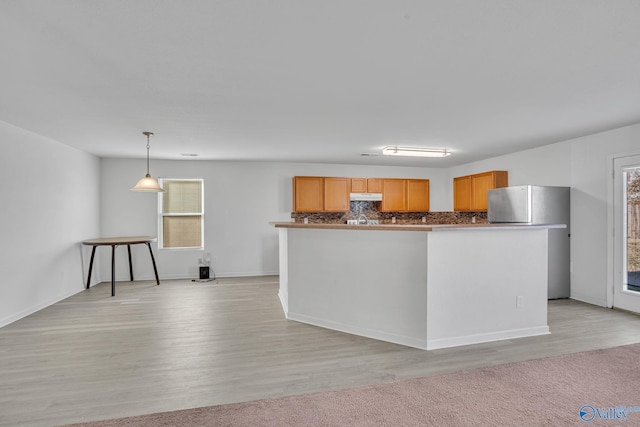 kitchen featuring backsplash, hanging light fixtures, stainless steel fridge, light wood-type flooring, and light brown cabinetry