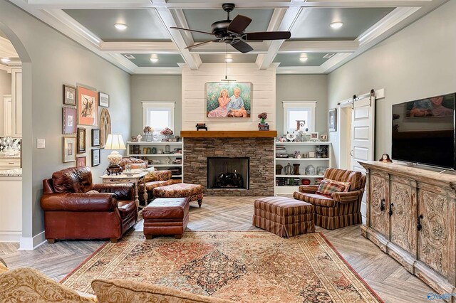 living area featuring arched walkways, a barn door, baseboards, ceiling fan, and a stone fireplace