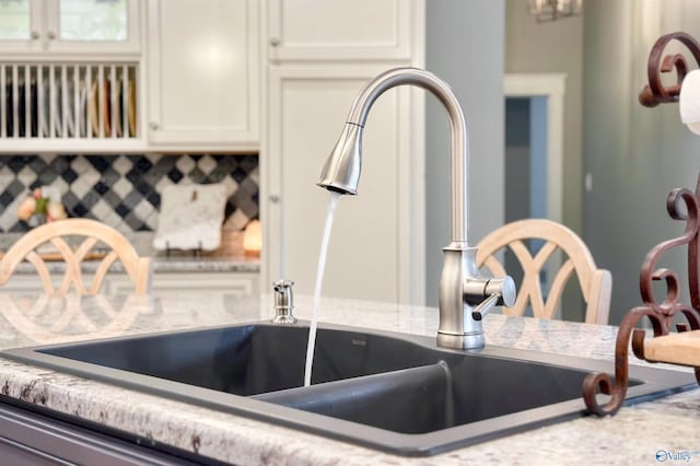 room details with light stone counters, glass insert cabinets, white cabinetry, and a sink