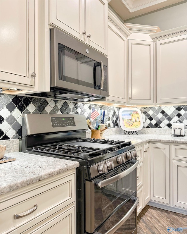 kitchen featuring light wood finished floors, stainless steel appliances, backsplash, and ornamental molding