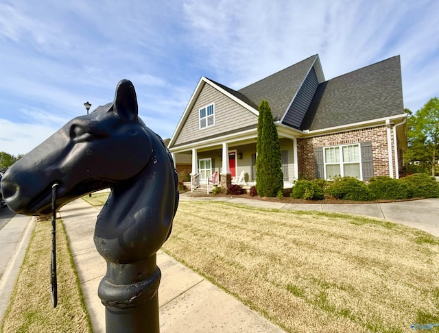 view of front of property featuring a front lawn, brick siding, a porch, and a shingled roof