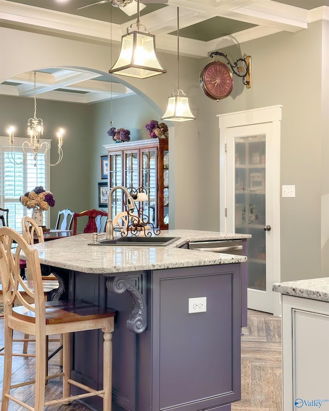 kitchen featuring coffered ceiling, light stone counters, a sink, and pendant lighting