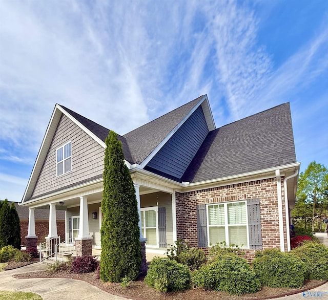 view of front facade featuring brick siding, a shingled roof, and covered porch