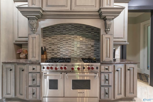 kitchen featuring dark stone countertops, tasteful backsplash, range with two ovens, and light tile patterned floors