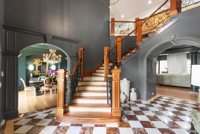 stairway featuring a towering ceiling, wood-type flooring, decorative columns, ornamental molding, and a chandelier