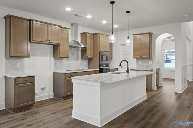 kitchen featuring an island with sink, light stone countertops, black electric stovetop, oven, and wall chimney range hood