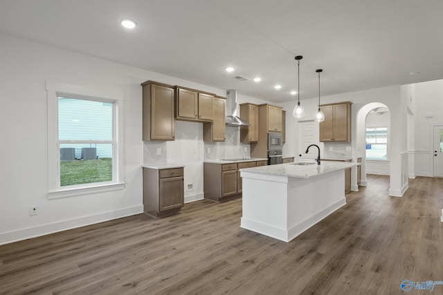 kitchen featuring decorative light fixtures, sink, stainless steel appliances, a center island with sink, and wall chimney exhaust hood