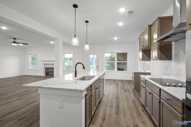 kitchen featuring sink, black electric stovetop, a center island with sink, decorative light fixtures, and wall chimney exhaust hood