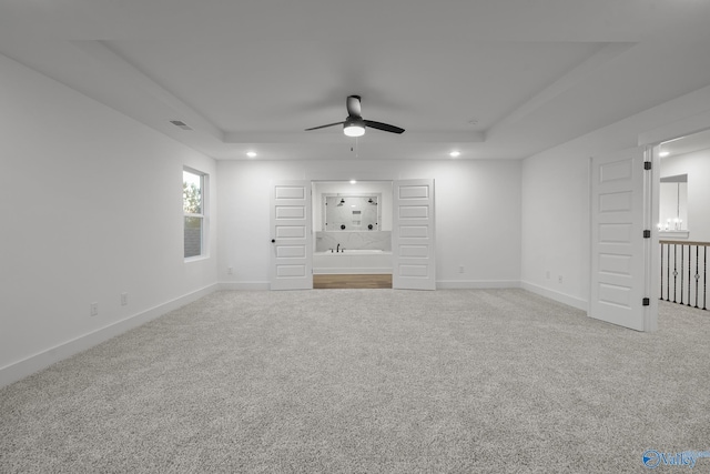 unfurnished living room featuring a raised ceiling, ceiling fan, and carpet