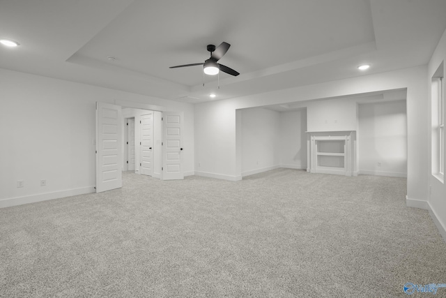 unfurnished living room with ceiling fan, light colored carpet, and a tray ceiling