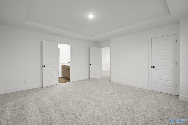 unfurnished bedroom featuring light carpet, a tray ceiling, and ensuite bath