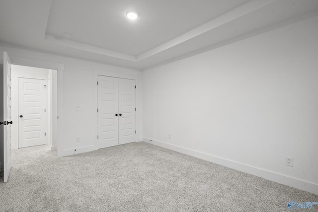 unfurnished bedroom with a closet, carpet flooring, and a tray ceiling