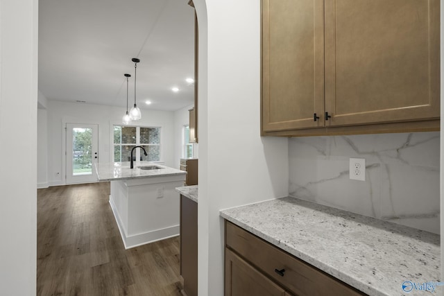 kitchen featuring light stone countertops, sink, pendant lighting, and decorative backsplash