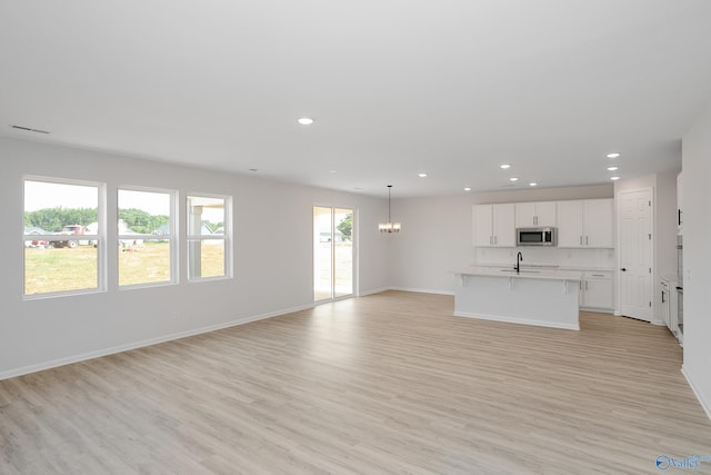 unfurnished living room with sink, a chandelier, and light hardwood / wood-style flooring