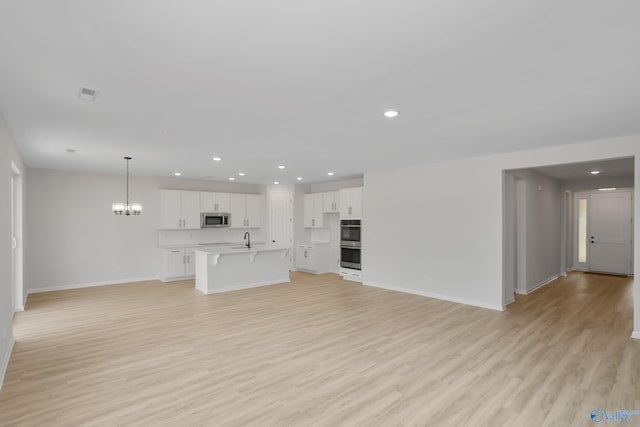 unfurnished living room with sink, a notable chandelier, and light hardwood / wood-style floors