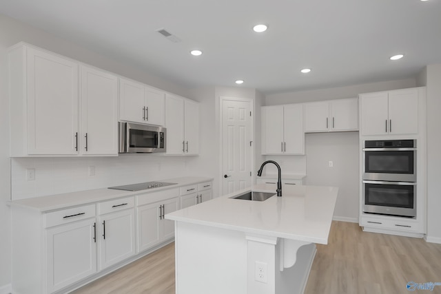 kitchen with sink, light hardwood / wood-style flooring, appliances with stainless steel finishes, an island with sink, and white cabinets