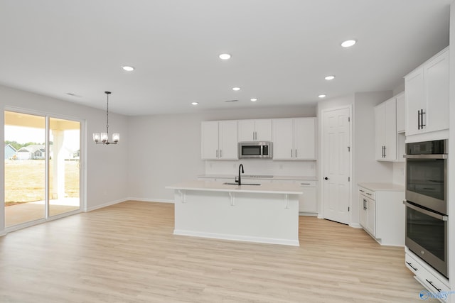 kitchen with a kitchen island with sink, stainless steel appliances, tasteful backsplash, white cabinets, and light wood-type flooring