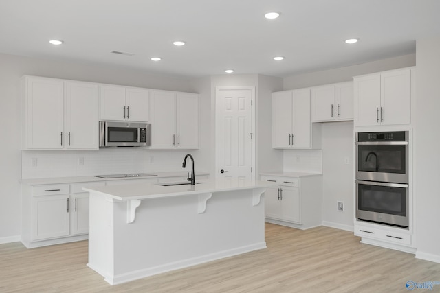 kitchen with stainless steel appliances, an island with sink, sink, and white cabinetry