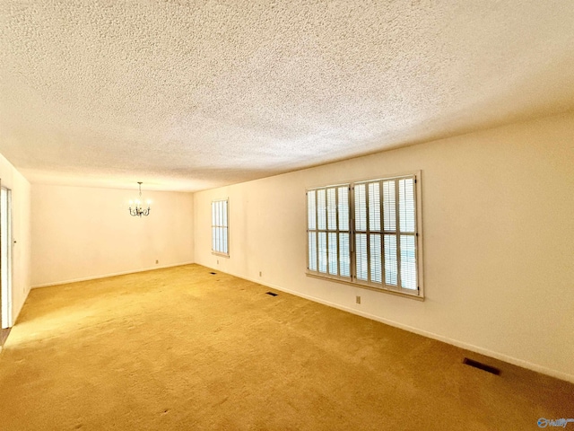 unfurnished room with carpet, a textured ceiling, and a chandelier