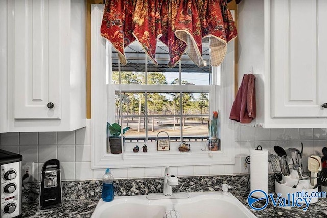 interior space with white cabinetry, sink, decorative backsplash, and dark stone countertops