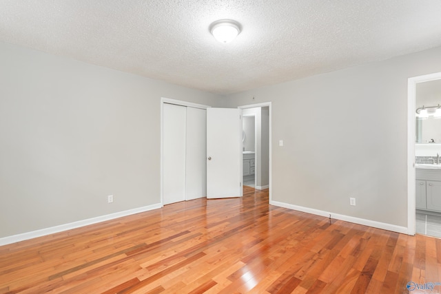 unfurnished bedroom with ensuite bath, hardwood / wood-style floors, a textured ceiling, and a closet