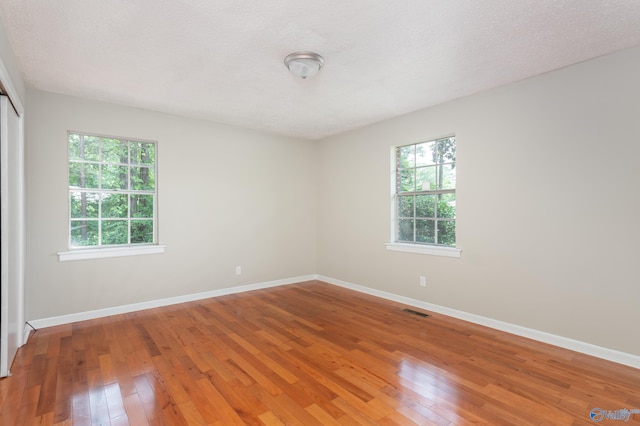 spare room with a textured ceiling, wood-type flooring, and a healthy amount of sunlight