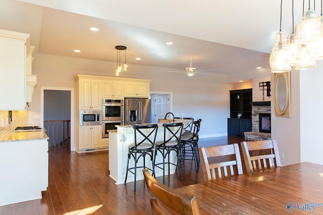 kitchen featuring pendant lighting, dark wood-type flooring, a breakfast bar area, appliances with stainless steel finishes, and light stone counters