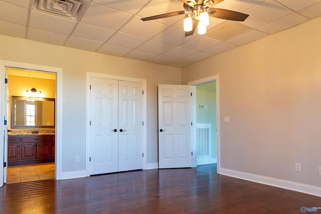 unfurnished bedroom with dark wood-type flooring, ensuite bathroom, a closet, ceiling fan, and a drop ceiling