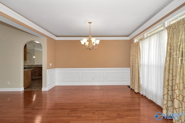 unfurnished room featuring arched walkways, a notable chandelier, wood finished floors, and ornamental molding