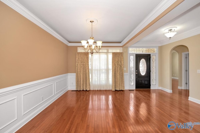 entrance foyer with wood finished floors, arched walkways, crown molding, a decorative wall, and a chandelier