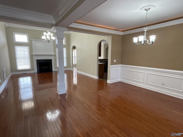 unfurnished living room featuring ornate columns, dark wood finished floors, an inviting chandelier, a fireplace with flush hearth, and ornamental molding