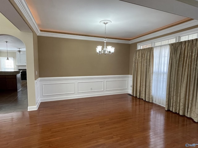 spare room with dark wood-type flooring, ornamental molding, ceiling fan with notable chandelier, a fireplace, and arched walkways