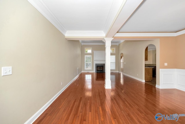 unfurnished living room with wood finished floors, baseboards, a fireplace, arched walkways, and crown molding