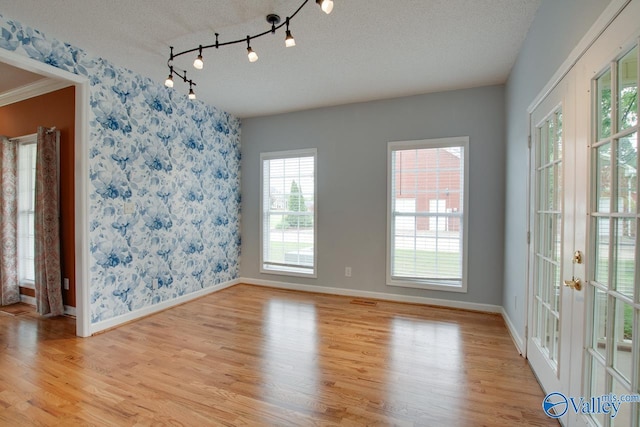 unfurnished dining area featuring a textured ceiling, wallpapered walls, and light wood-type flooring