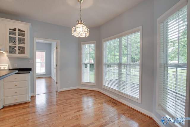 unfurnished dining area with light wood-style floors, baseboards, and an inviting chandelier